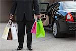 Chauffeur holds shopping bags in driveway near luxury vehicle