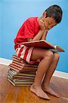 Boy reading while seated on stack of books