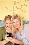 Two young women using mobile phone in bedroom