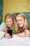 Two young women using mobile phone in bedroom