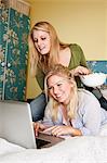 Two young women using laptop in bedroom
