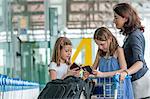 Mère et filles debout à l'extérieur de l'aéroport avec des bagages
