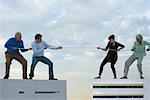 Oversized men and woman standing on rooftops, playing tug-of-war