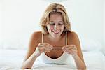 Young woman lying on bed looking at pregnancy test, smiling