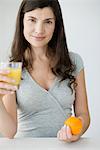 Mid-adult woman holding glass of orange juice and fresh orange