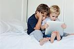 Jeunes frères assis sur le lit regardant la tablette numérique