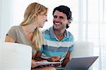 Couple shopping online with laptop, looking at each other laughing