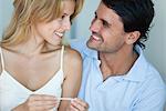 Couple smiling at each other, woman holding pregnancy test