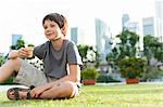 Boy sitting on grass in park, city skyline in background