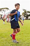 Boy carrying soccer balls on pitch