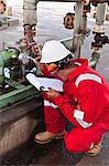 Worker noting gauge at oil refinery