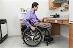 Man in wheelchair with spinal cord injury opening a drawer in an accessible kitchen