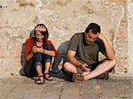 Italy, Venice, Mature couple leaning against wall, texting with mobile phones