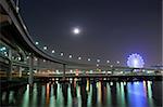 hanged-up highway road over Tokyo bay waters at night time with moon and ferris-wheel illumination on backward