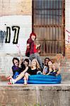 Crazy teen punks sit together in an inflatable pool behind an old warehouse downtown.