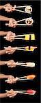 Set of 7 hands holding various types of sushi with chopsticks isolated on a black background.