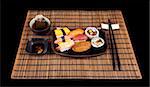 Single setting of sushi and tea on a bamboo mat isolated on black.