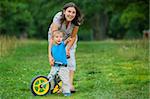 Portrait of little boy on a bicycle and his mother in the summer park