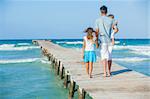 Family of three on wooden jetty by the ocean. Back view