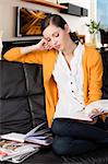 young girl student sitting on a sofa and reading a book, her elbow is resting on the back of the sofa and she watches the book with absorbed expression.