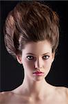 close up portrait of young beautiful woman with dark hair and creative hairstyle posing an black background