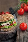 Delicious ham, cheese and salami sandwich with vegetables, lettuce, cherry tomatoes in natural setting with wooden background