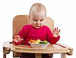 young child in red shirt eating vegetables in wooden chair.