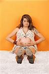 Pregnant lady in pain with hands on tummy sitting on floor