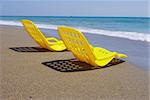 Two empty plastic chairs stand under sunbeams in  day-time on sand