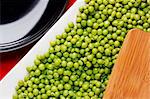 Directly above photograph of an edge of a cutting board and green peas.