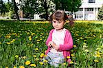 A smiling girl sitting on the dandelion field wearing a pink shirt