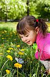 A smiling girl wearing a pink shirt, sitting on the dandelion field and observing a butterfly