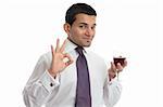 A man holding a glass of wine makes a hand sign to show approval, or excellence.  White background.