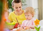 Mom helping baby painting on Easter eggs