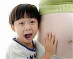A shot of a little surprising Asian boy listening to her pregnant mother belly