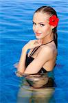 Tropical girl with flower on her ear posing in swimming pool