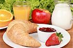 French breakfast with a croissant and strawberry jam. Served with milk, fresh orange juice, an orange and an apple.