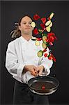 Photo of a young chef with dreadlocks tossing chopped vegetables in the air from a frying pan.