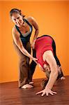 Yoga instructor helping student stretch over orange background