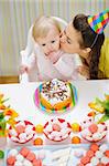 Mother kissing baby eating birthday cake