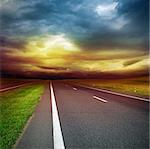 asphalt road in the field over stormy dark cloudy sky - sunset in the evening