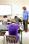 Students taking a standardized test as a teacher looks on to ensure no cheating.