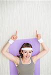 Happy young woman laying on fitness mat and pointing on copy space