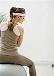 Woman sitting on fitness ball back to camera and looking on copy space