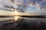 The sun rising behind clouds is reflected in the water of the marshes near the Bodie Island lighthouse at Cape Hatteras National Seashore on the Outer Banks of North Carolina