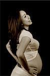 Asian pregnant lady standing on black background, sepia tone.