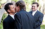 Wedding of handsome gay male couple.  The grooms kiss as the minister looks on.