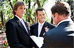 Handsome gay male couple getting married by a minister in beautiful outdoor setting.