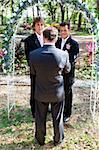 Gay male couple getting married in a beautiful garden setting underneath a floral archway.