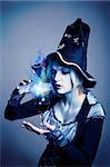 Pretty young witch in black and silver costume conjuring with a potion